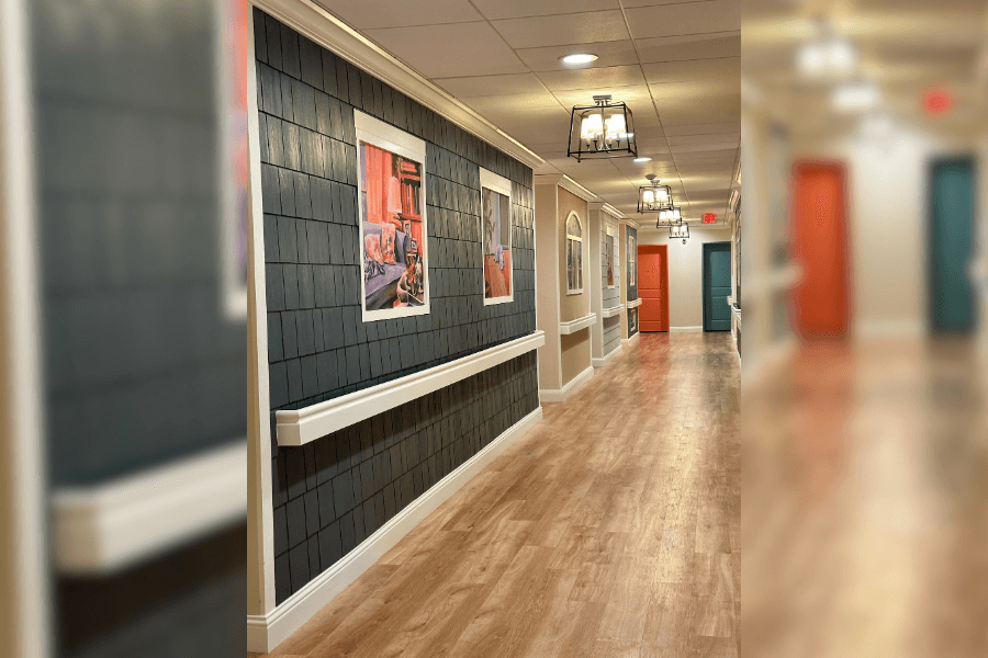 Modern hallway with dark shingle walls, framed artwork, wood floors, pendant lights, and colorful doors.