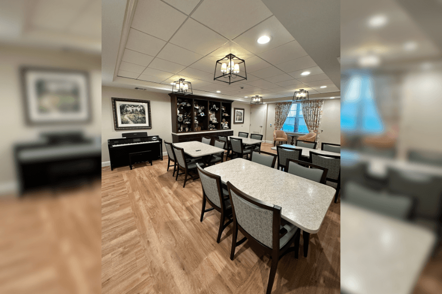 Dining room with tables, upholstered chairs, a piano, hutch, and pendant lighting on wood flooring.