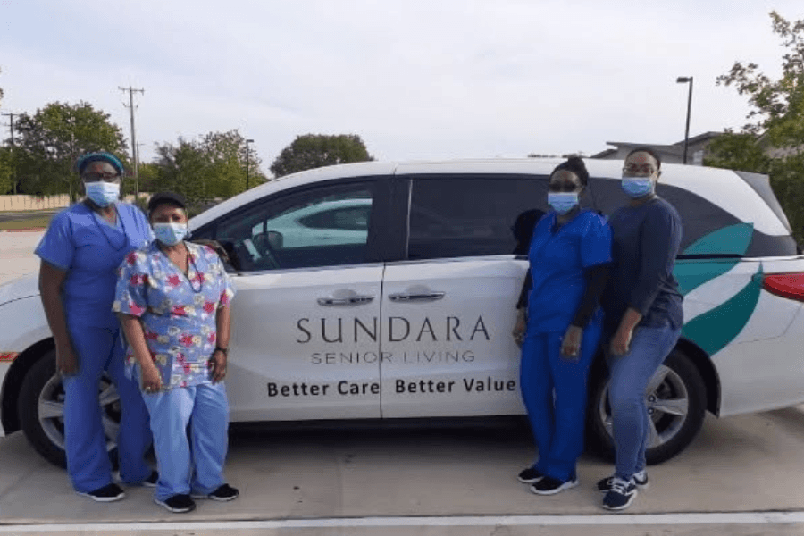 Four masked staff in scrubs stand beside a white Sundara Senior Living van reading "Better Care, Better Value.