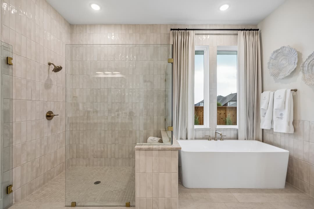 Modern bathroom with walk-in glass shower, freestanding tub by curtained window, and white towels on wall.