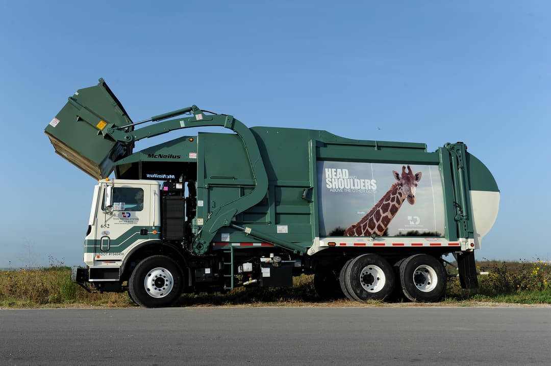 Green Texas Disposal Systems garbage truck with giraffe ad reading "Head and Shoulders Above the Other Guys.