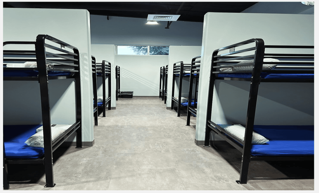 Rows of black metal bunk beds with blue mattresses and pillows in a shelter dormitory.
