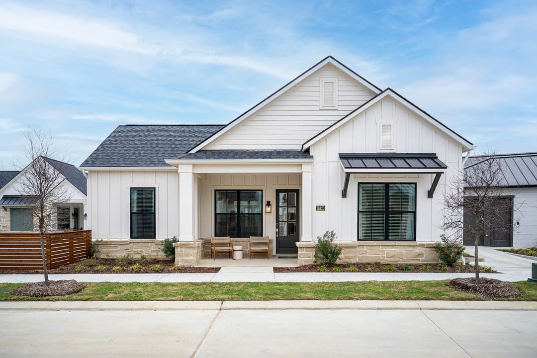 Modern white farmhouse-style home with black windows, stone accents, and a covered porch with two chairs.