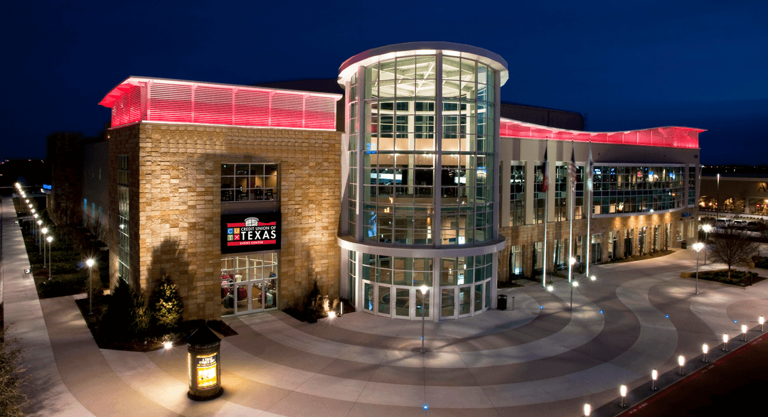 Credit Union of Texas Event Center at dusk, featuring a curved glass entrance and red-lit stone facade.