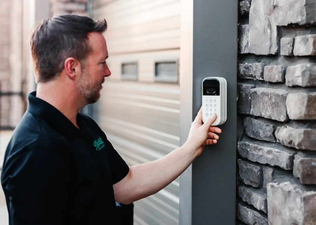 Man in black polo entering a code on a keypad access panel with camera mounted on a stone wall.