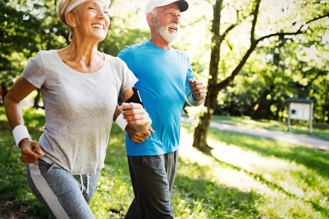 Smiling senior couple jogging together through a sunlit green park.