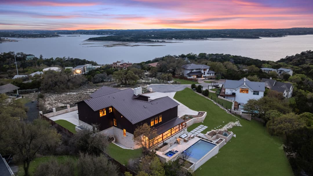 Aerial view of modern lakeside home with pool at sunset, overlooking a large lake and hillside neighborhood.