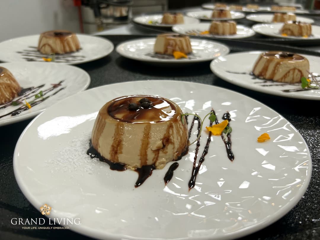 Plated flan desserts drizzled with chocolate sauce and garnished with edible flowers, lined up for service.