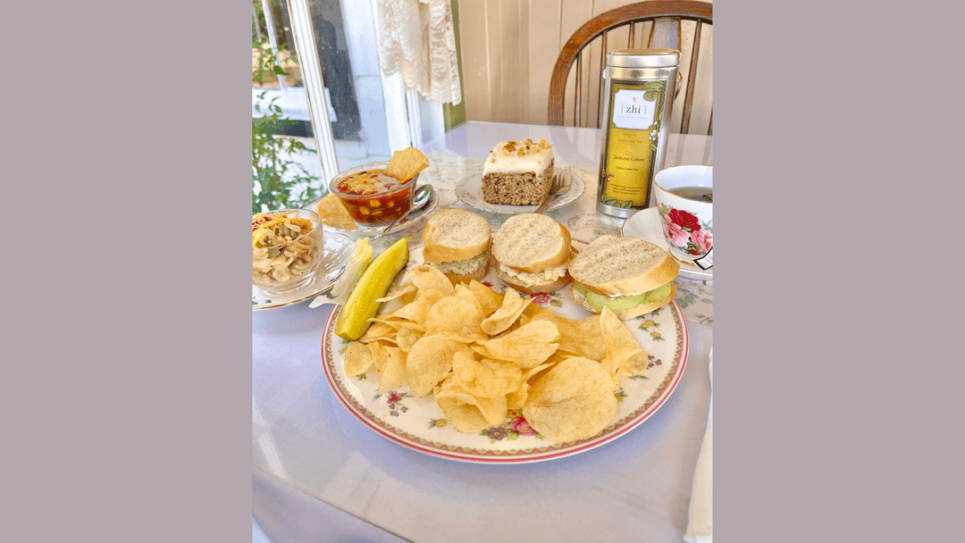 Tea room lunch with sliders, chips, pickle, cake, tea in floral china, and a tin of Jasmine Green loose leaf tea.