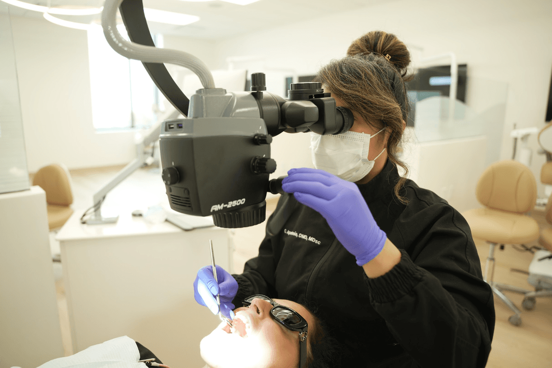Dentist using a dental microscope to examine a patient's teeth in a bright clinic.