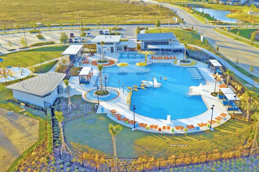 Aerial view of a community pool complex with lounge chairs, cabanas, palm trees and modern buildings.
