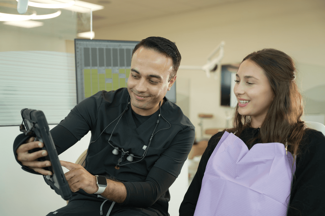 Dentist showing tablet to a smiling patient wearing a purple bib in a dental office.