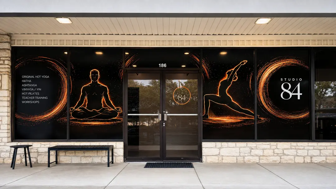Storefront of Studio 84 yoga with glowing figures on windows, class list, and address 186 above glass doors.