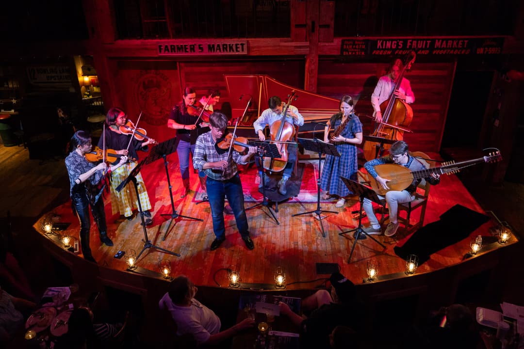 A chamber orchestra standing on a wooden stage.
