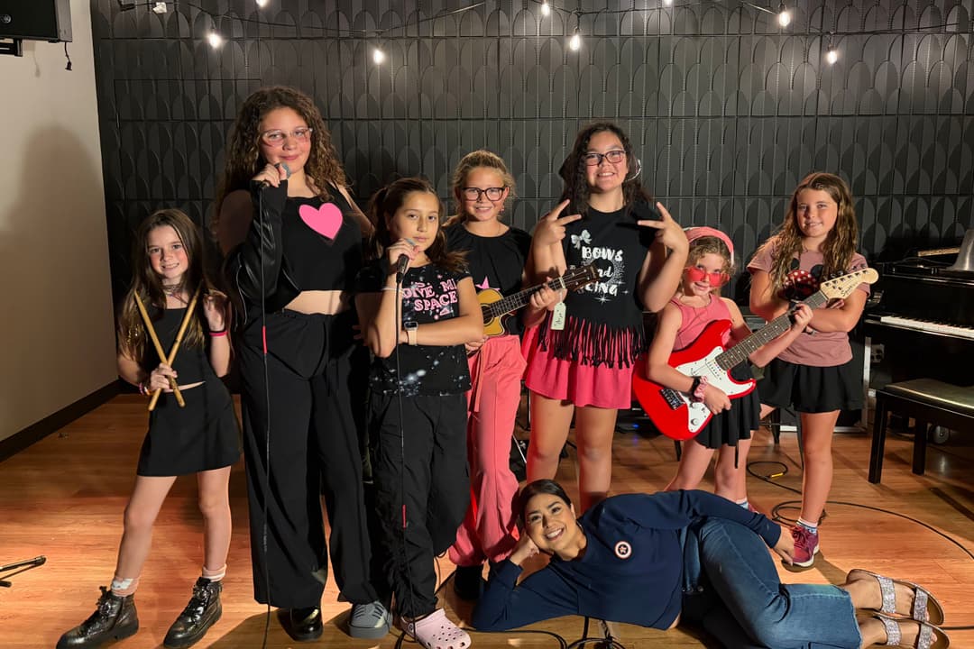 Group of young girls posing with instruments in a music studio, with an adult reclining in front.