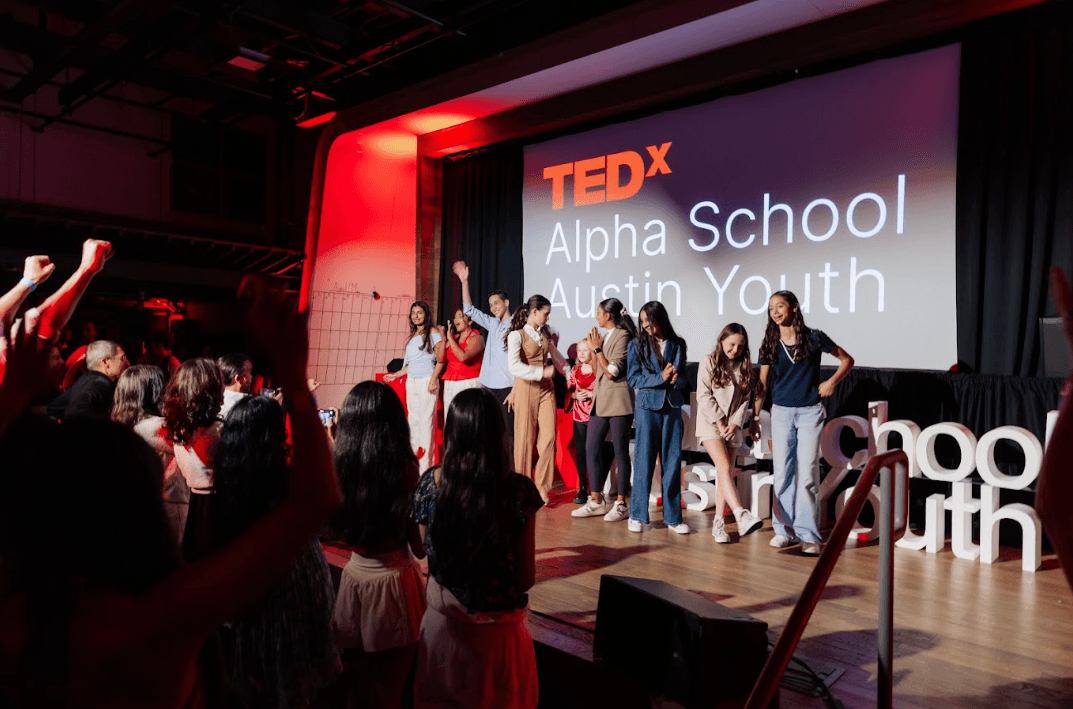 Young speakers stand on stage before a TEDx Alpha School Austin Youth screen as an audience applauds.