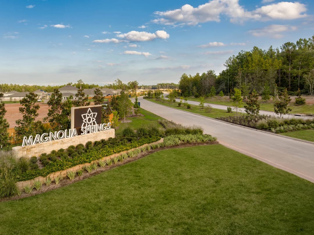 Magnolia Springs stone entrance sign with landscaped gardens beside a road leading into a residential community.