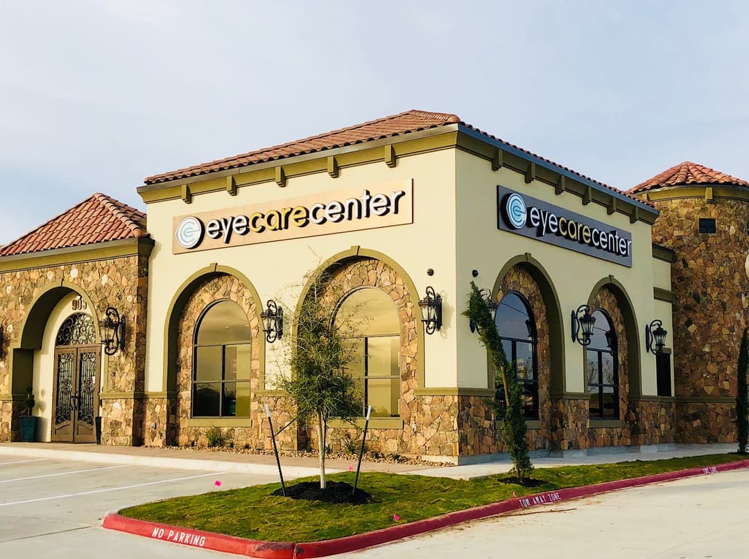 Stone and stucco building with tile roof, arched windows and two "eyecarecenter" signs, beside an empty parking lot.