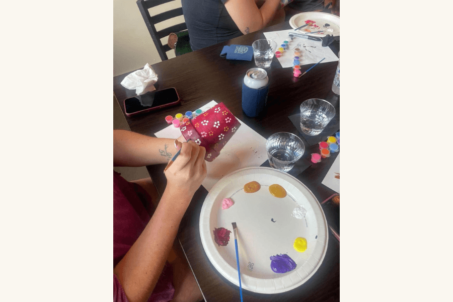 Person painting flowers on a small box, using paint dabs on a paper plate palette at a table.
