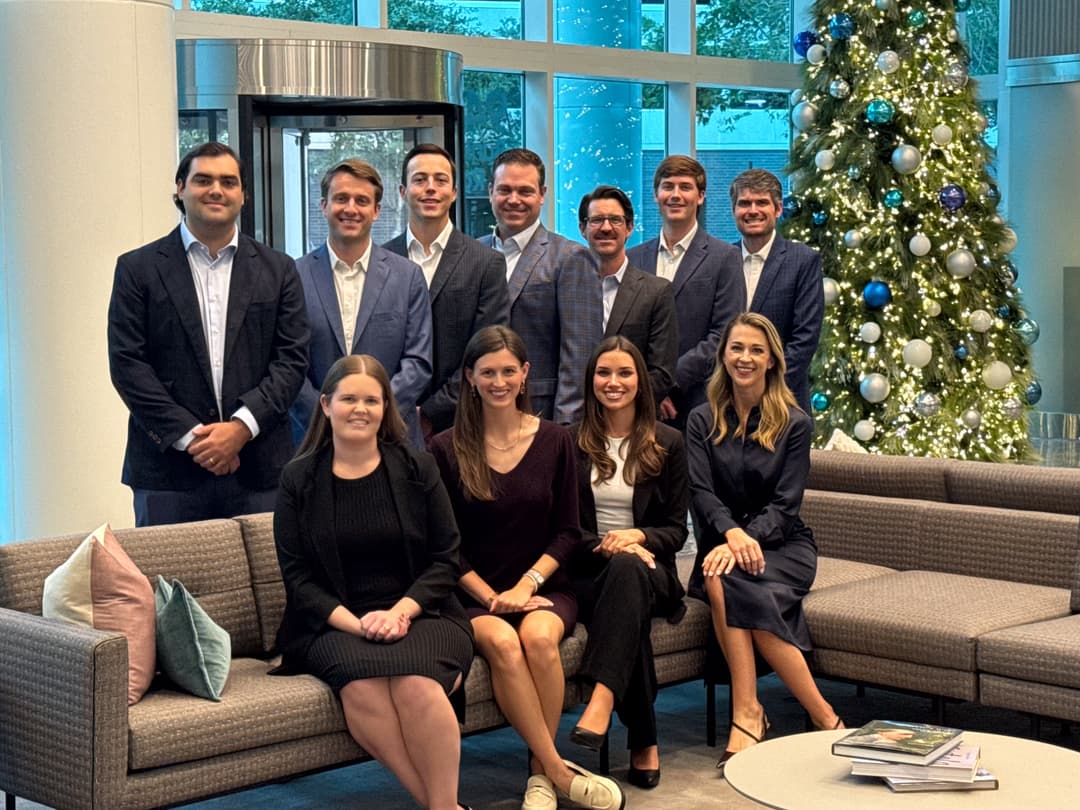 Business team poses in an office lobby beside a decorated Christmas tree, women seated on a couch and men standing behind.
