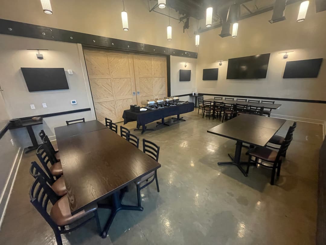 Private event room with wooden tables, chairs, buffet setup, TVs on walls, and a sliding barn door.