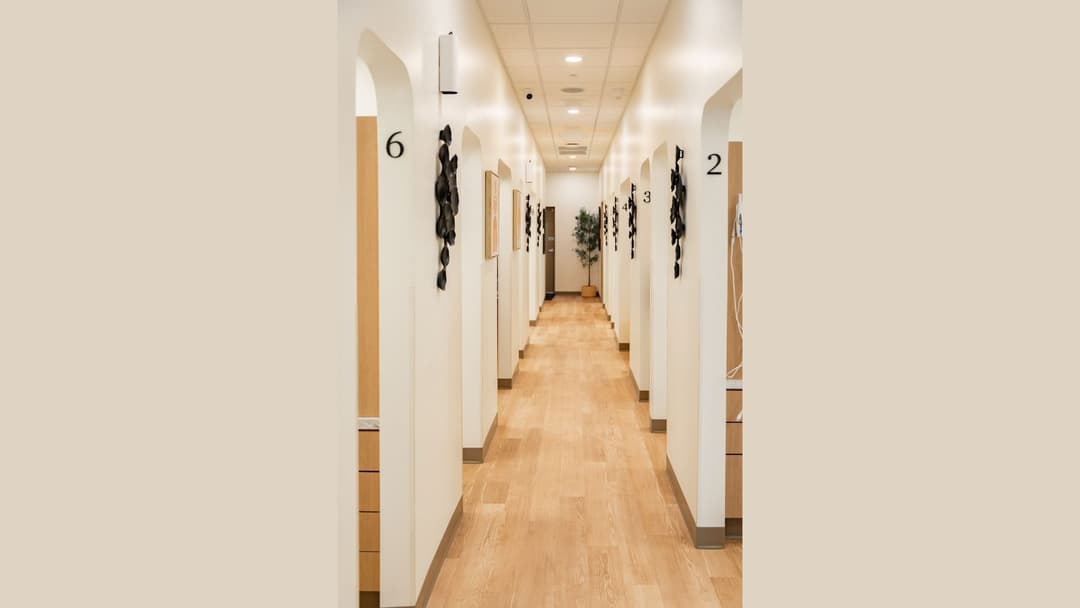 Modern medical clinic hallway with numbered arched treatment bays, wood floors, and wall art.