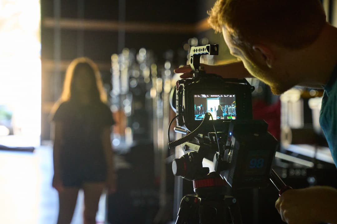 Videographer operating a professional camera on tripod, filming a woman standing at a bar.