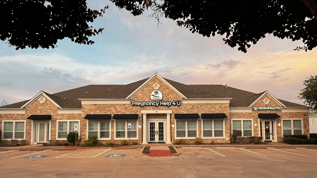 Stone office building with "Pregnancy Help 4 U" sign and empty parking lot at dusk.