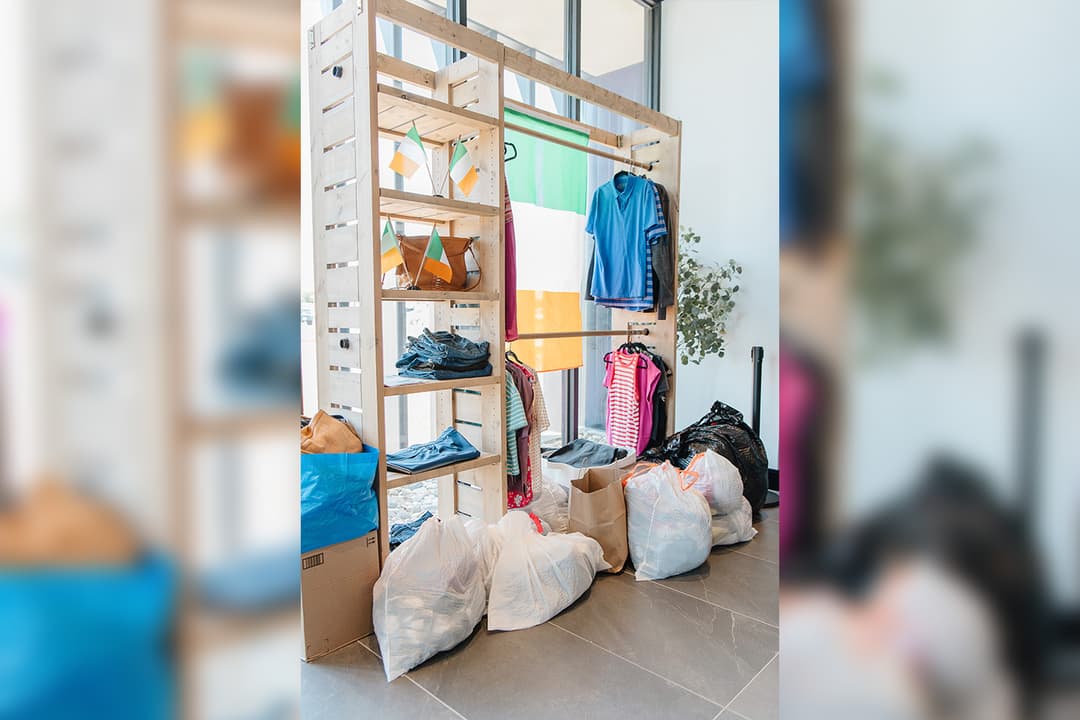 Donated clothes on a wooden rack with Irish flags, and bags of clothing on the floor at a collection point.