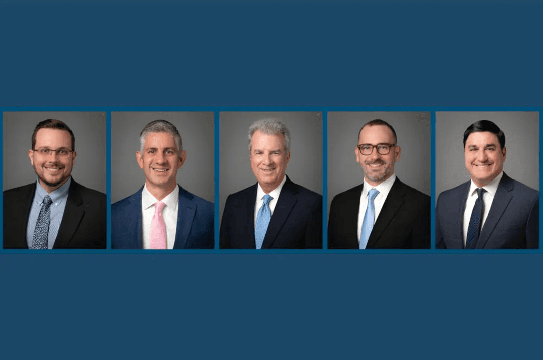 Five men in business suits and ties smiling in professional headshots on a blue background.
