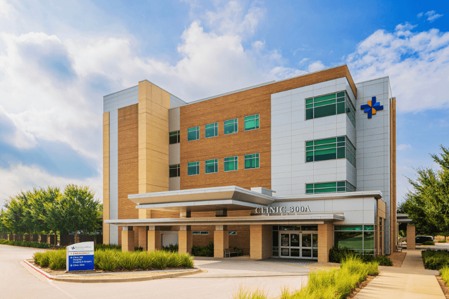 Modern four-story medical clinic building labeled "Clinic 300A" with brick and white facade under a blue sky.