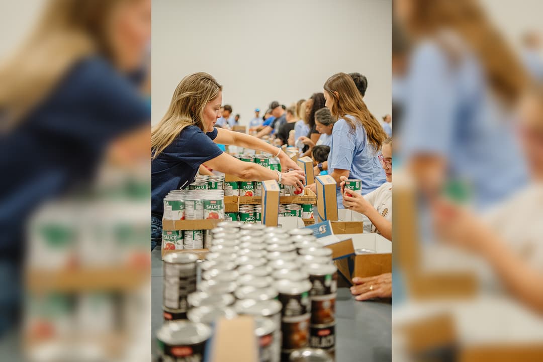 Volunteers sort canned goods into boxes at a food drive packing event.