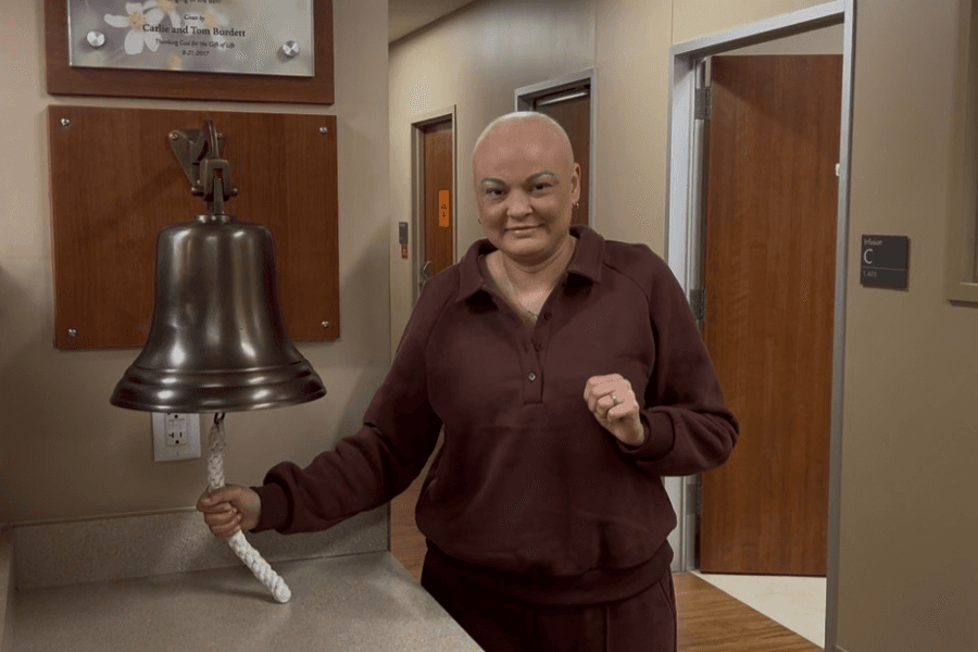 Smiling woman rings a bronze bell to mark the end of cancer treatment at a medical facility.