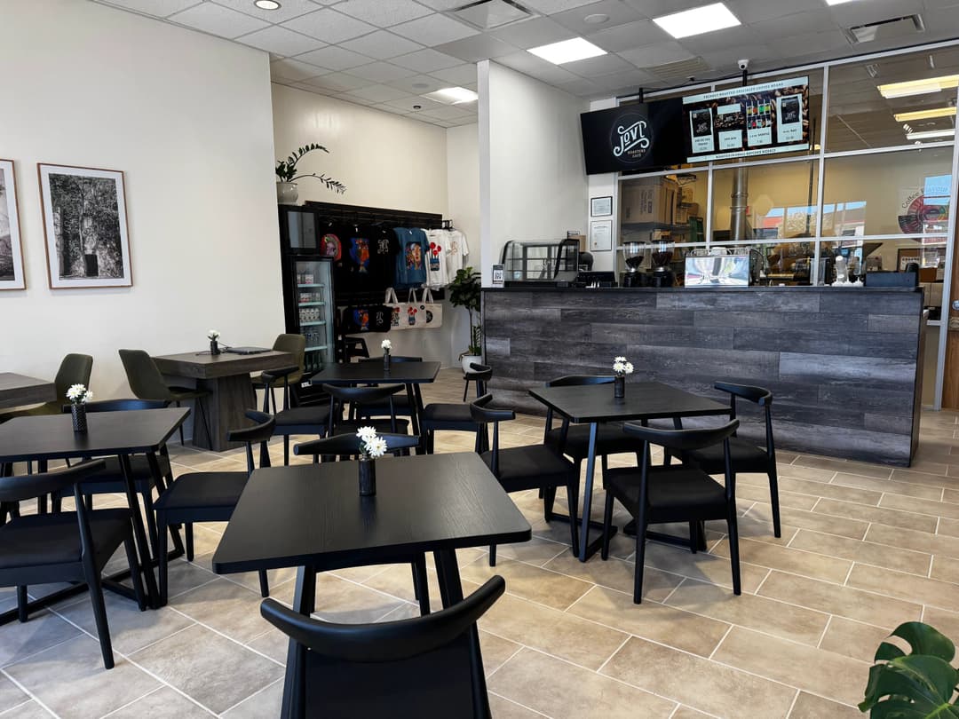 Interior of Jovi Roasters Café with black tables and chairs, service counter, menu screen, and merchandise display.