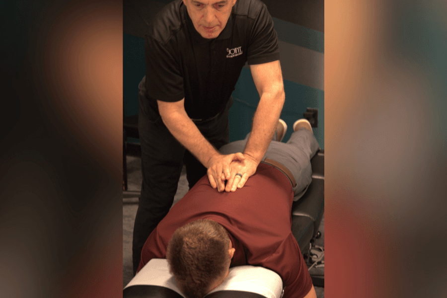 Chiropractor adjusting the lower back of a patient lying face down on a treatment table.