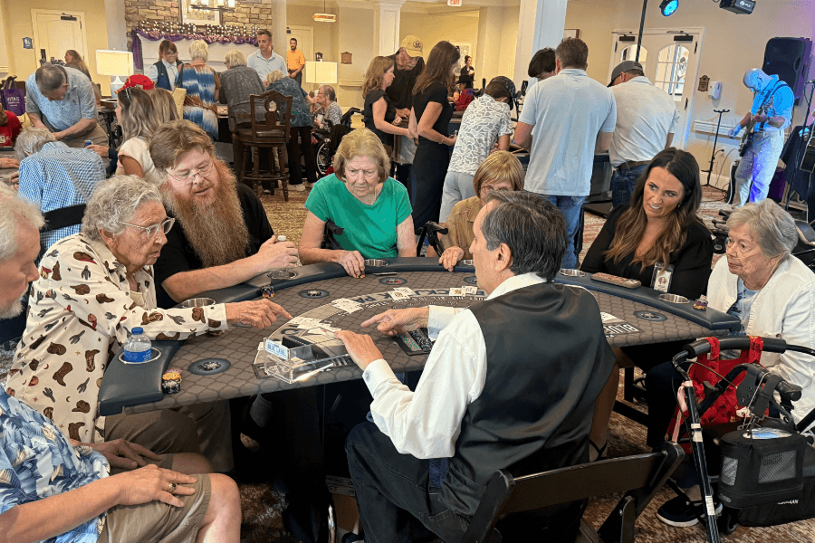 Dealer in vest runs a casino-style card game table for seniors at a crowded indoor community event.
