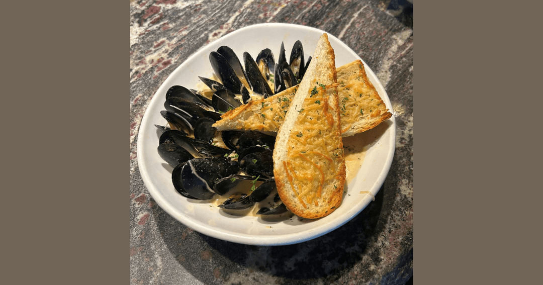 Bowl of mussels in cream sauce served with toasted cheese bread on a stone table.