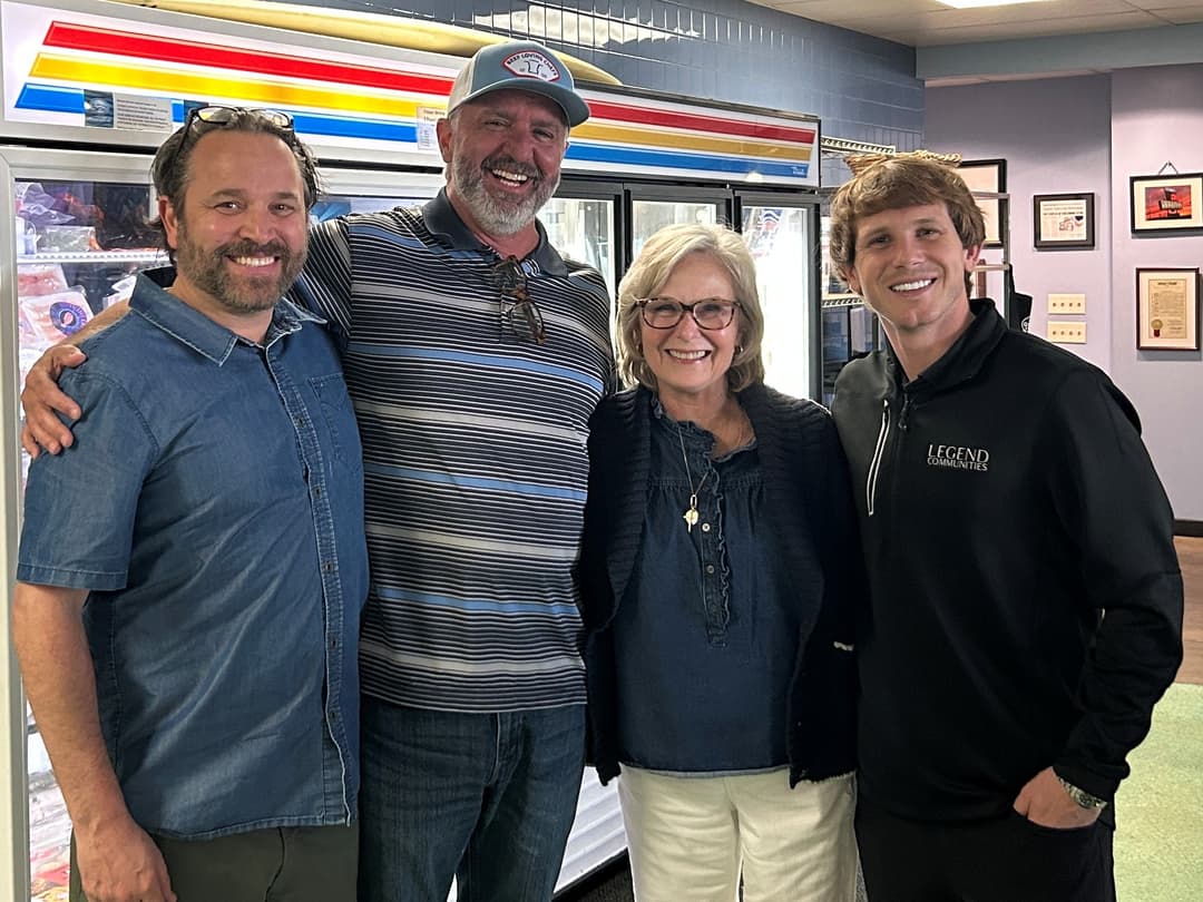 Four people smiling together in a store with refrigerated display cases behind them.