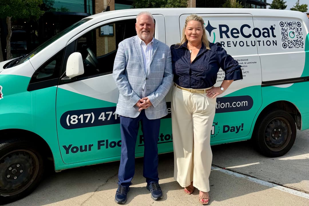 A man and woman stand smiling in front of a teal and white ReCoat Revolution branded work van.
