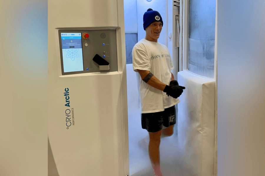 Man in beanie, t-shirt and shorts stands inside a Cryo Arctic whole-body cryotherapy chamber with cold mist.