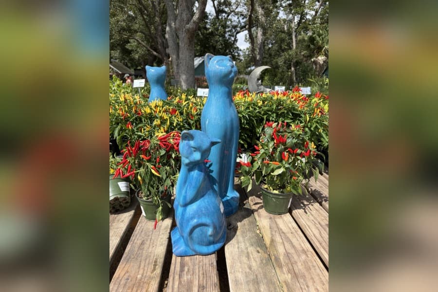 Blue ceramic cat statues on a wooden table in front of potted ornamental pepper plants at a nursery.