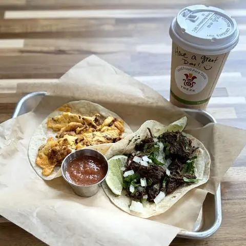 Two tacos with salsa and lime on a metal tray beside a coffee cup reading "Have a great day.