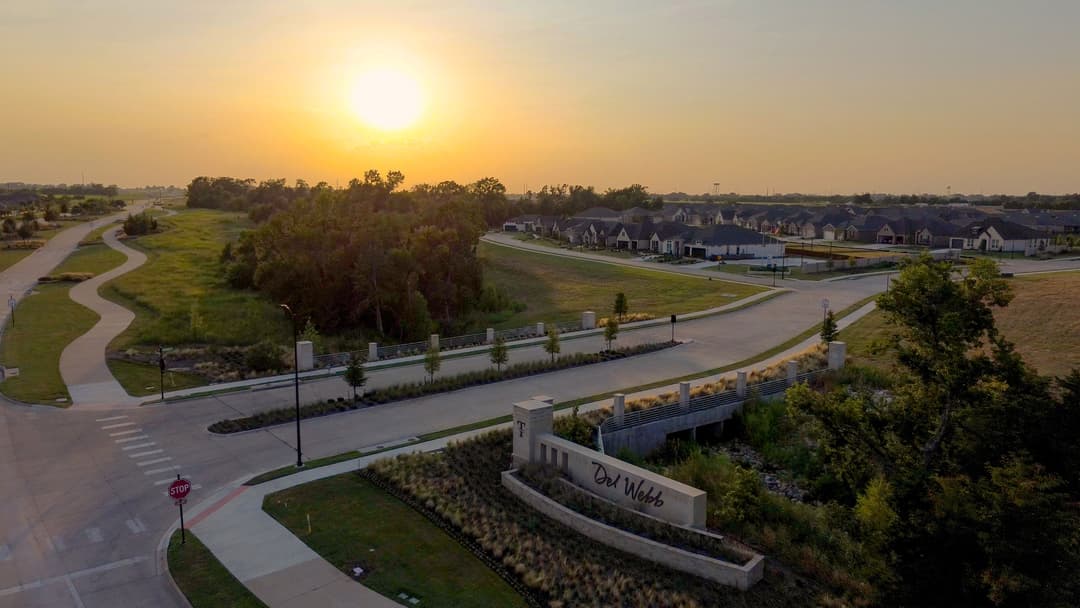 Aerial view of Del Webb community entrance at sunset, with winding roads and rows of houses.