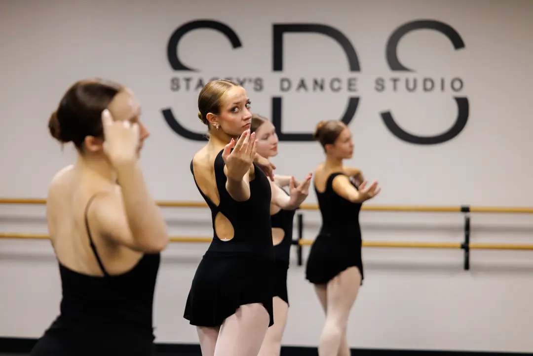 Three dancers in black leotards practice at Kingwood Ballet with one dancer looking at the camera.