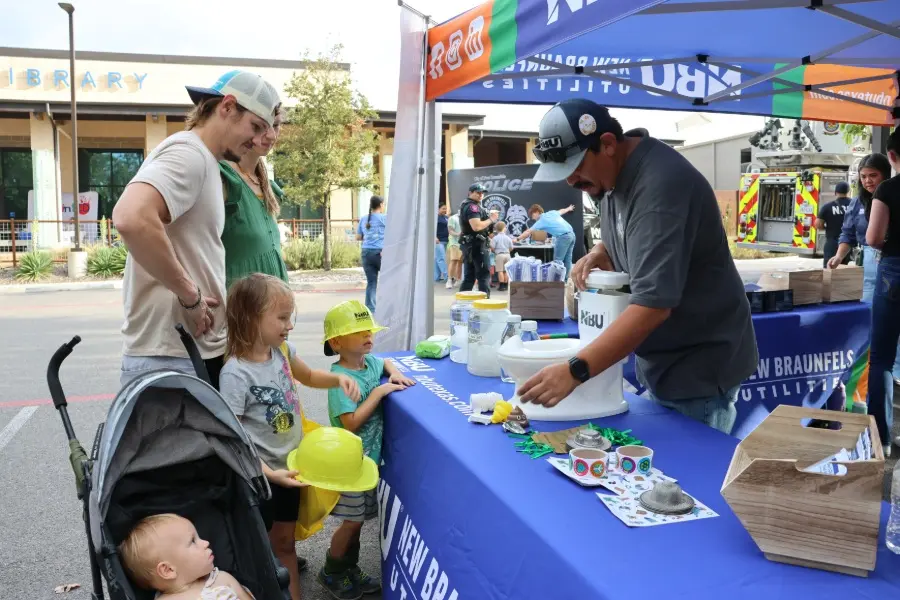 A family with young children visits a New Braunfels Utilities booth at a community outdoor event.