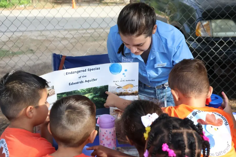 A woman in a blue NBU shirt teaches children about endangered species of the Edwards Aquifer using a poster.