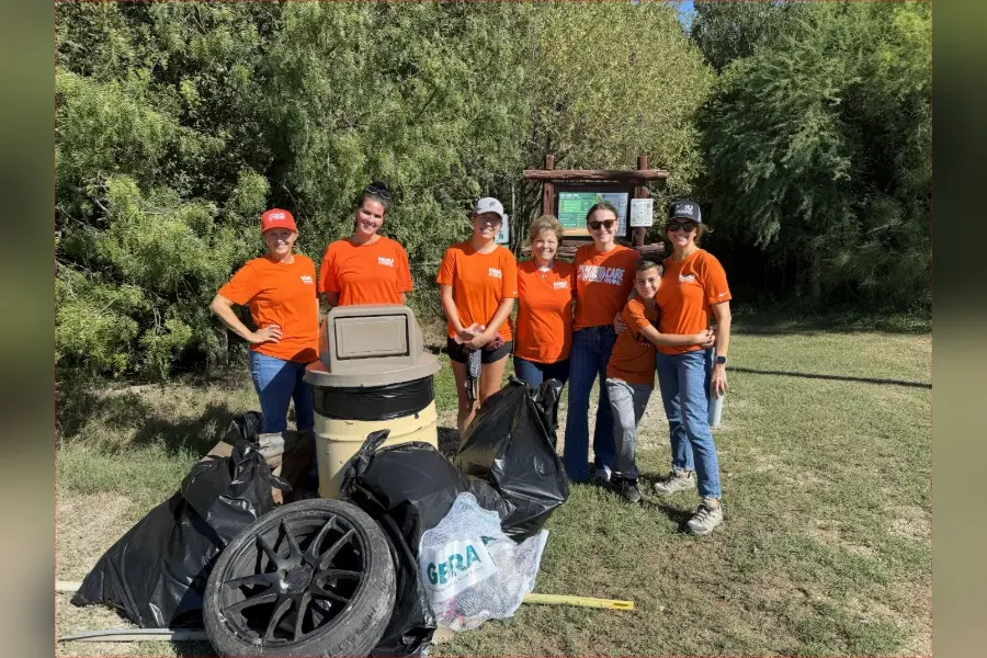 Group of volunteers in orange shirts stand behind trash bags and tires collected during an outdoor cleanup.