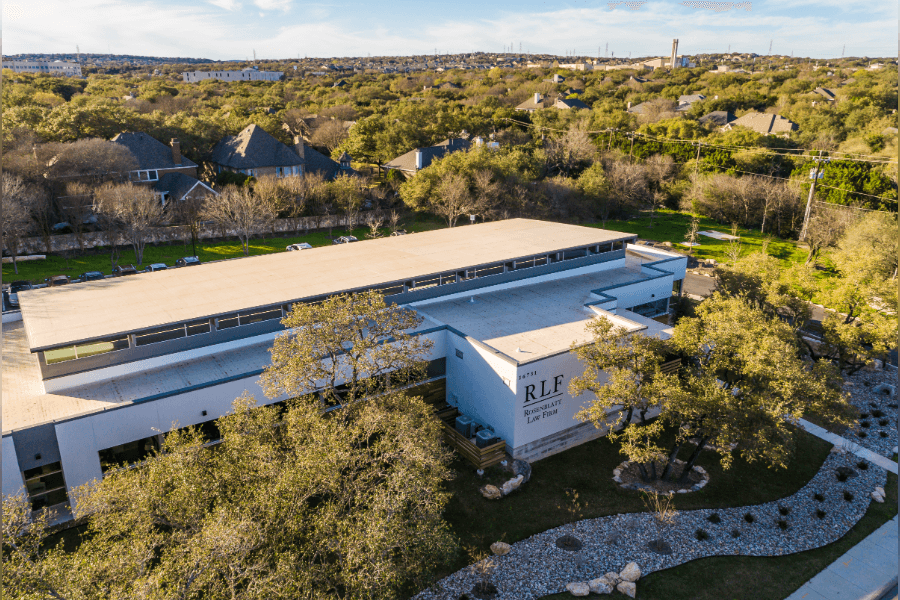 Aerial view of modern white office building marked "RLF" surrounded by trees and suburban homes.