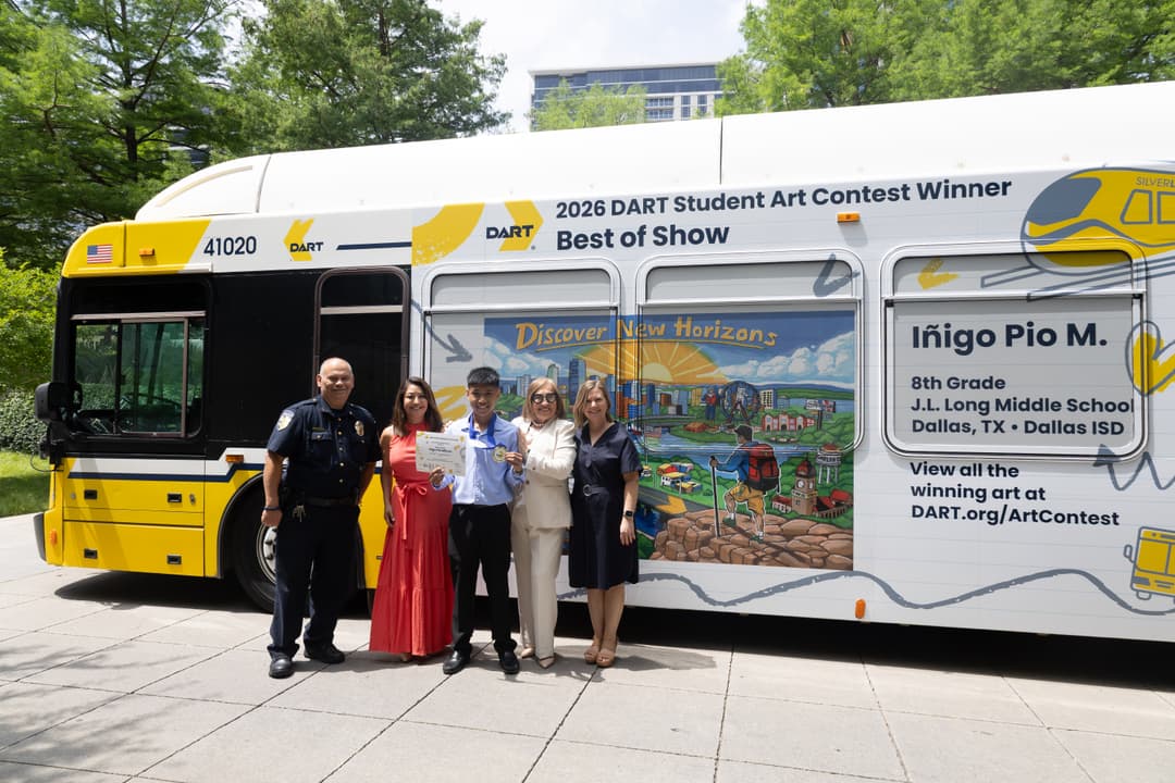 The winner of A student art contest and members of DART stand in front of a DART bus with his artwork on the side of the bus