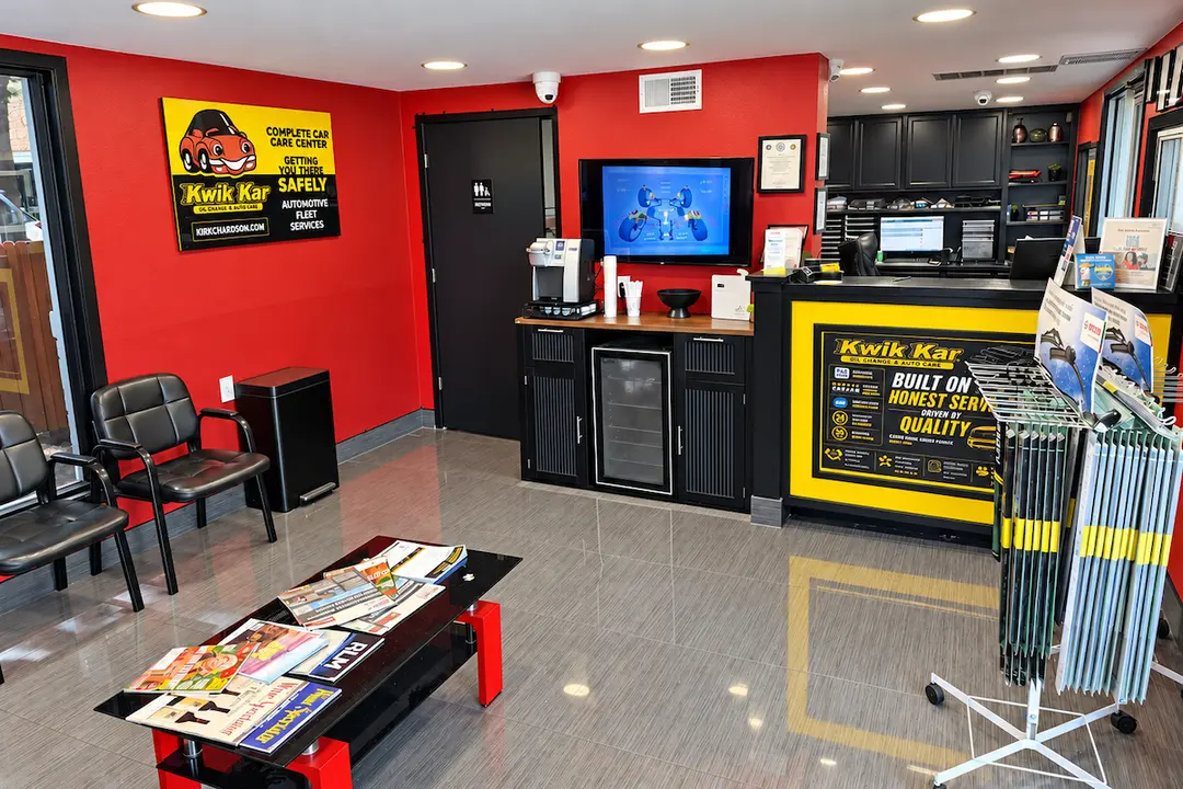 Kwik Kar auto care waiting room with red walls, black chairs, magazine table, service counter and coffee station.